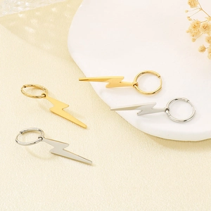 Detailed macro view of polished gold and silver lightning bolt earrings on a ceramic dish