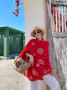 Detail of red beach shawl with gold print paired with a straw sun hat and bag