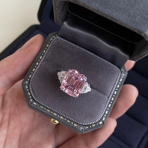 Close-up of emerald cut pink gemstone ring with side diamonds in a gray velvet jewelry box