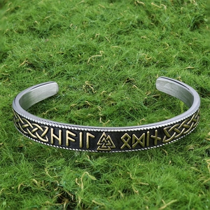 Detail of Viking open cuff bracelet with engraved golden runes on mossy background