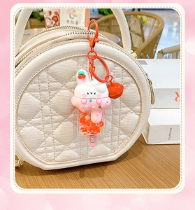 Detail of pink rabbit ice cream keychain with a red bell hanging on a quilted bag