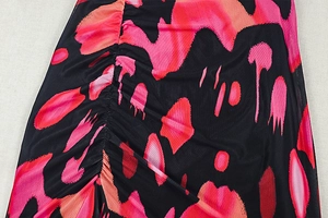 Detail of ruched black fabric with vibrant pink and orange gradient splatter pattern