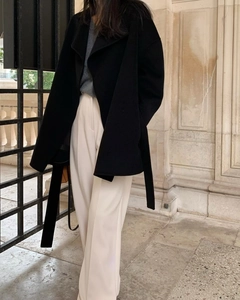 Detail of a black long wool coat with lapel and waist belt paired with beige trousers