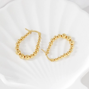 Macro detail of gold-plated beaded geometric earrings on a white shell texture tray
