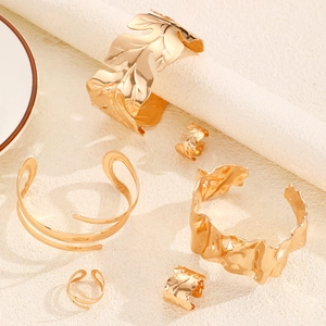 Detalle de brazaletes y anillos dorados con diseño de hoja de arce y ondas de estilo étnico