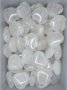 Close-up of numerous 2cm heart-shaped natural white crystal stones in a clear bowl