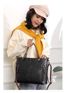Detail of black PU leather tote with brown straps and side zipper on a model