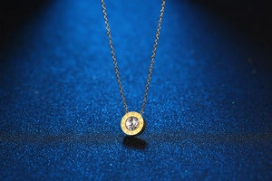 Macro detail of gold necklace with Roman numerals engraving and a central zircon stone