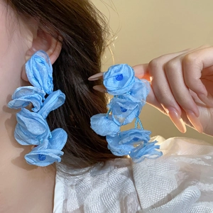 Close-up of blue floral drop earrings made of layered fabric on a female model