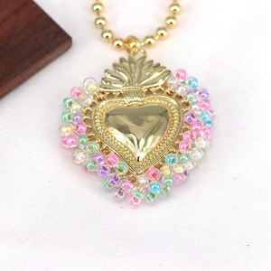 Macro shot of gold sacred heart pendant with colorful beads and crown detail on gold chain