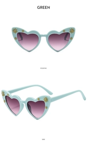 Detail view of heart-shaped green sunglasses with gold daisies and gradient lenses