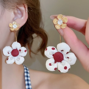 Macro detail of long floral drop earrings with gold petals and white polka dot fabric