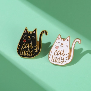 Pair of black and white cat lady enamel pins with gold trim on a green background