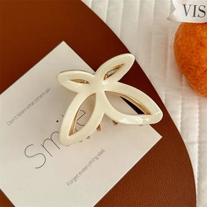Close-up of cream petal hair claw clip with golden metal accents on a display tray