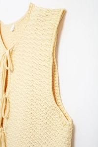 Detail of light yellow knit vest showing texture, V-neck, and delicate front tie closure