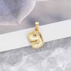 Macro detail of number 9 gold pendant featuring a textured honeycomb pattern design