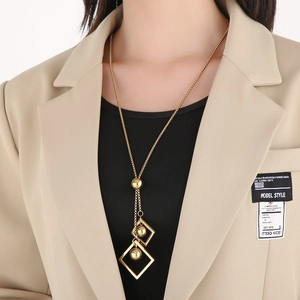 Detail of a gold geometric long necklace with square and spherical pendants on a model