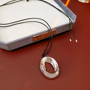 Detail of silver oval pendant with black braided cord on red leather jewelry display