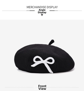 Detail view of a classic black knit beret with a stylish white bow embroidery detail