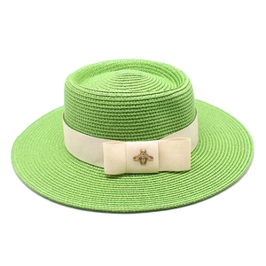 Detail of light green boater hat featuring beige ribbon bow and golden bee accessory