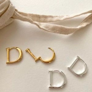Close-up of gold and silver D-letter earrings on beige fabric with cotton ribbon