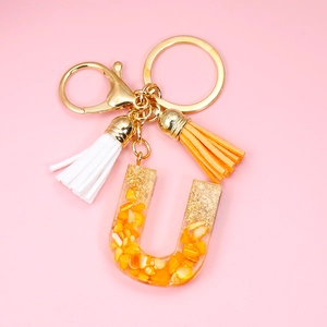 Detail of resin letter U keychain featuring gold foil flakes and colorful tassels