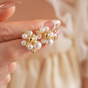 Dettaglio degli orecchini a fiore con perle, metallo dorato e zirconi in mano