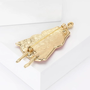 Detail of gold metal brooch back showing textured character shape and secure safety pin