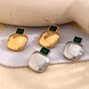 Detail of square gold and silver earrings with green emerald zircon on textured surface