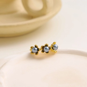Elegante anello a fiore dorato con tre perle blu-grigio su un piatto di ceramica