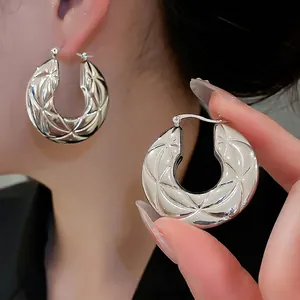 Polished silver hoop earrings with starburst geometric texture worn by a model