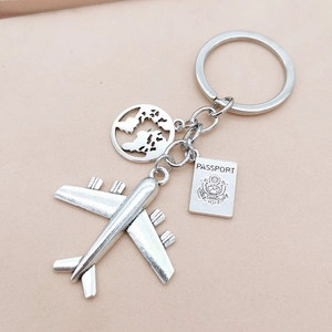Detail of travel keychain with silver airplane, globe, and passport charms on pink background