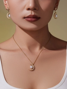 Dettaglio di un set di collana e orecchini dorati con luna, stella e perla indossato da modella