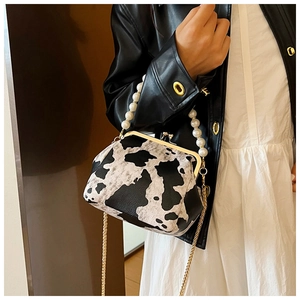 Detail of cow print handbag with elegant pearl handle and gold chain strap on a model