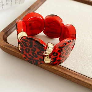 Close-up of red leopard print resin links and gold metal buckles on a wooden tray
