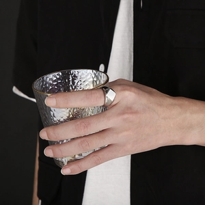 Detail of a geometric silver ring on finger holding a textured glass cup