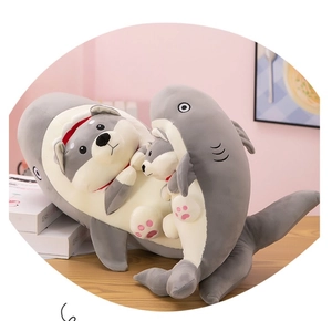 Detailed close-up of giant grey shark plush holding husky dog dolls in a home setting