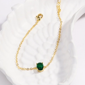 Close-up of gold-plated bracelet with an oval green zircon on a white textured tray