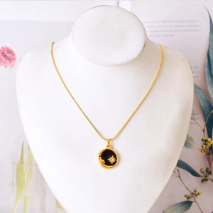 Golden starburst pendant necklace set with black enamel and zircon on a display stand