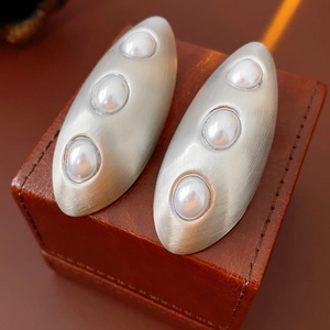 Vue macro de boucles d'oreilles ovales en argent brossé avec trois perles blanches