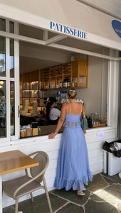 Back view of a blue backless maxi dress with tiered ruffles by a bakery storefront