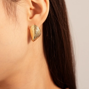 Detailed view of gold shell earrings with textured finish worn by a model