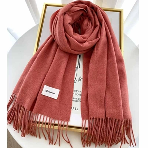 Close-up of thick solid color knit scarf with tassels and brand label hanging on frame