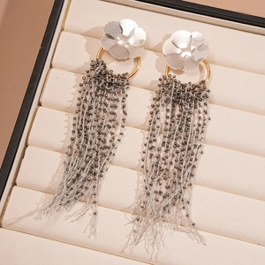 Detailed view of silver flower earrings with long beaded tassels in a jewelry box