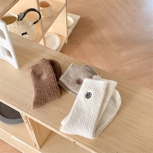 Close-up of three pairs of thick winter socks with delicate flower embroidery on wood