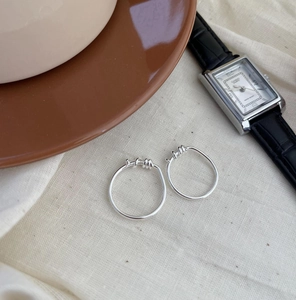 Minimalist silver hoop earrings with spiral detail on a textured linen background