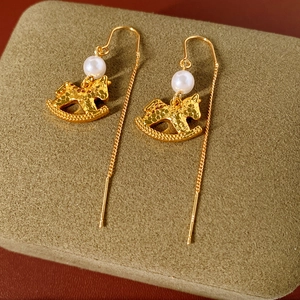 Detail of golden rocking horse earring with white pearl on green velvet display