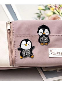 Close-up of cute penguin enamel pins with rhinestones pinned on a beige pencil case