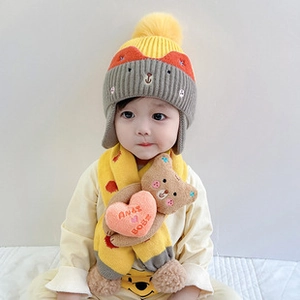 Detail of baby winter knit hat and scarf set with yellow pom-pom and bear patch