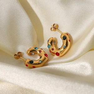 Detailed macro of gold C-shaped earrings with colorful gemstones on white silk